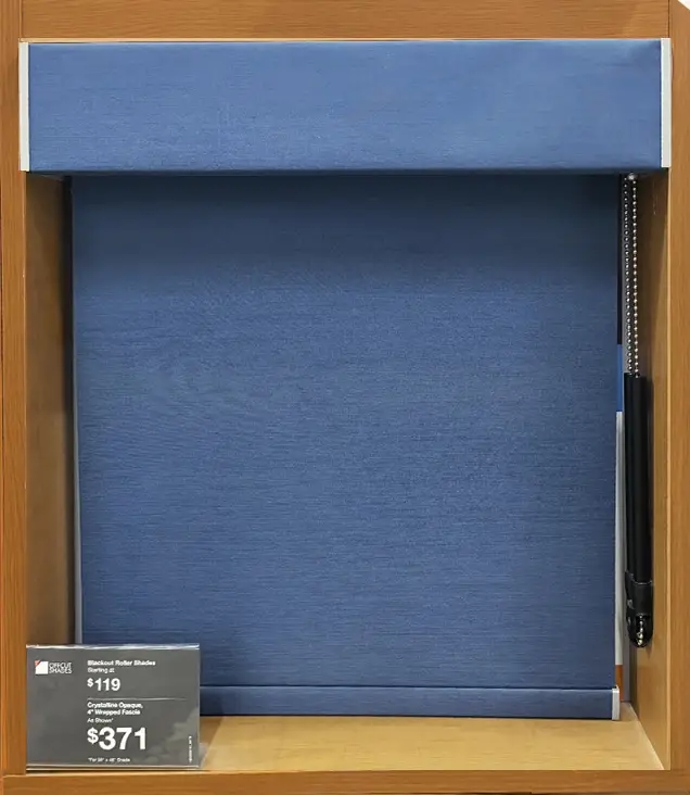 Blue blackout roller shade displayed in a wooden showroom frame with a chain-operated mechanism on the right side.