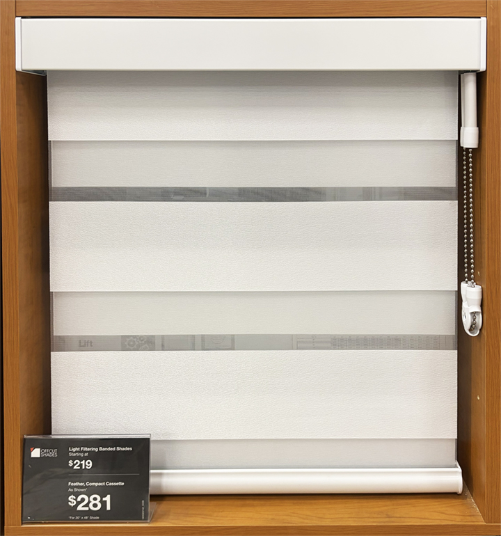 White banded/zebra roller shade with chain control displayed in a wood-framed showroom cabinet with a pricing tag reading $219 and $281