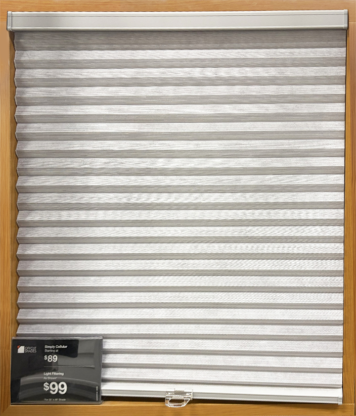 Gray cellular honeycomb shade displayed in a wood-framed showroom cabinet with a pricing tag reading $89 and $99