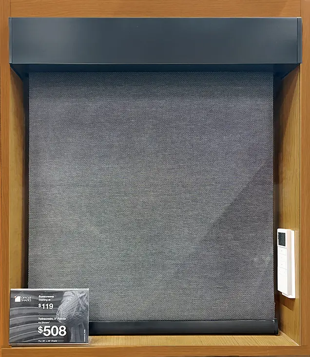 Gray roller window shade sample mounted in a wooden display frame with black top and bottom rails.