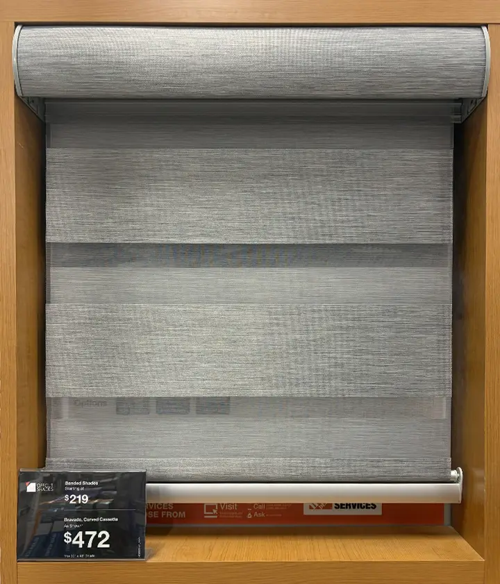 Gray banded/zebra roller shade displayed in a wood-framed showroom cabinet with a pricing tag reading $219 and $472