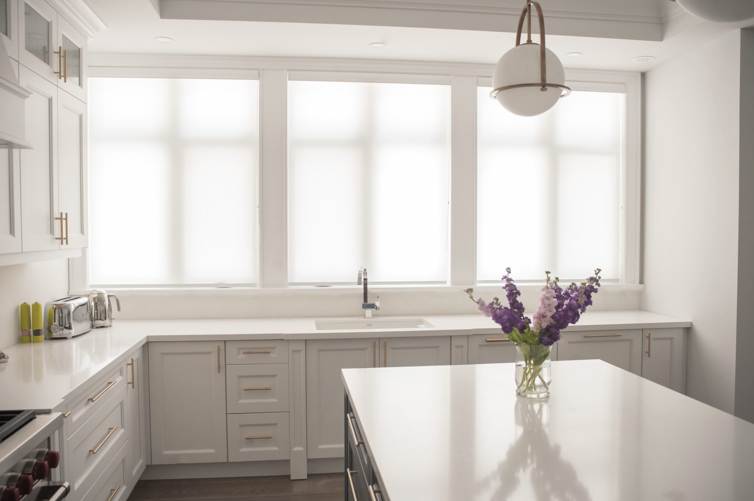 Bright white kitchen with custom roller shades filtering daylight across three large windows